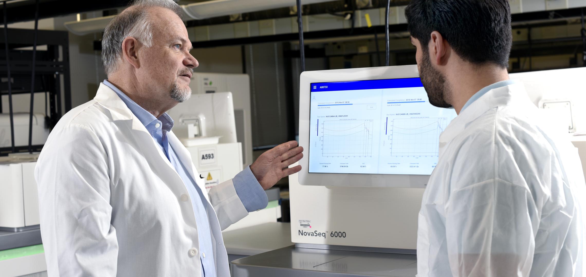 Two researchers reviewing genomic sequencing data on an Illumina NovaSeq 6000 instrument in a laboratory